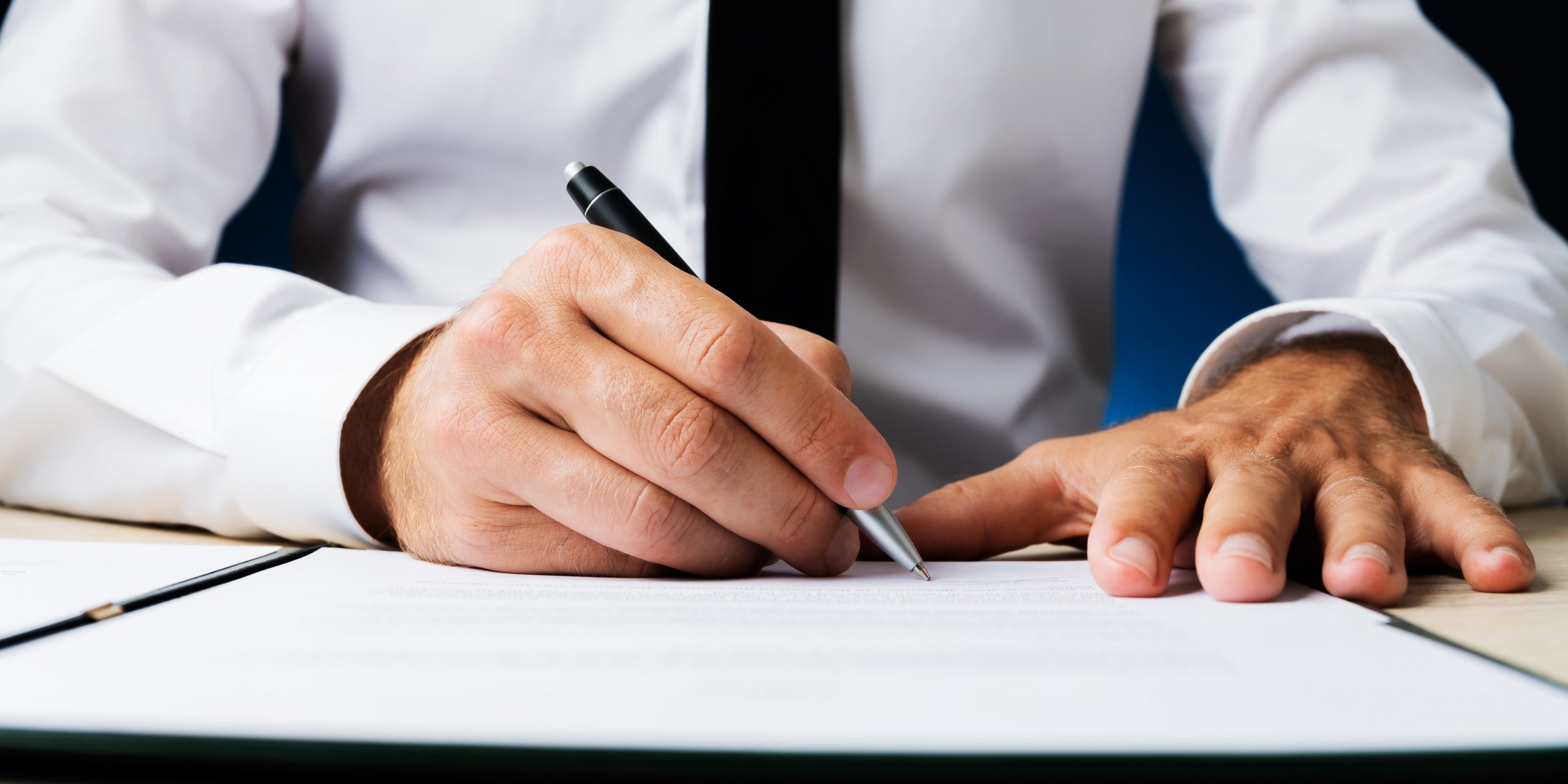 Wide view closeup image of businessman signing a document or contract.
